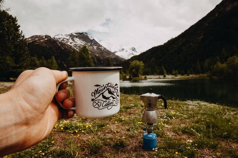 Hand holding cool retro enamel coffee cup up against a beautiful river and mountain vista