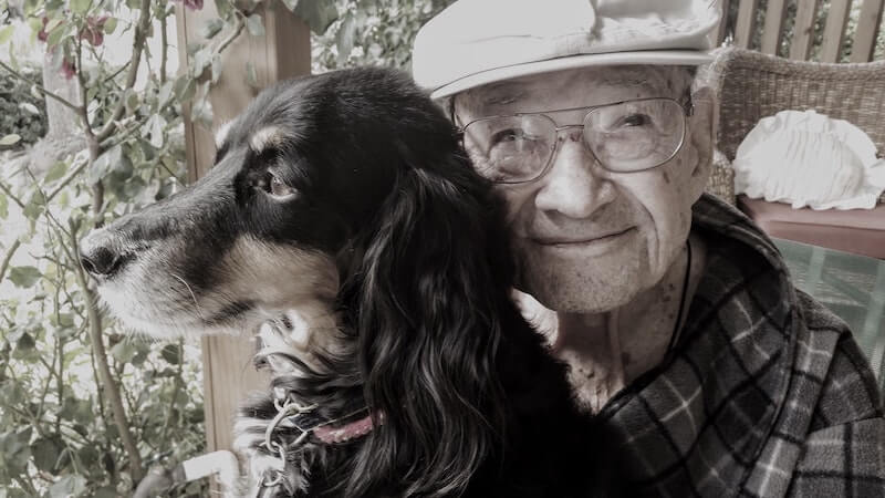 Smiling elderly man with black and tan dog.