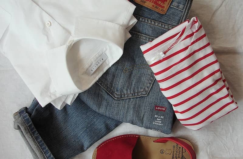 Women's clothing laid out: jeans, white shirt, striped t-shirt, and red sandals
