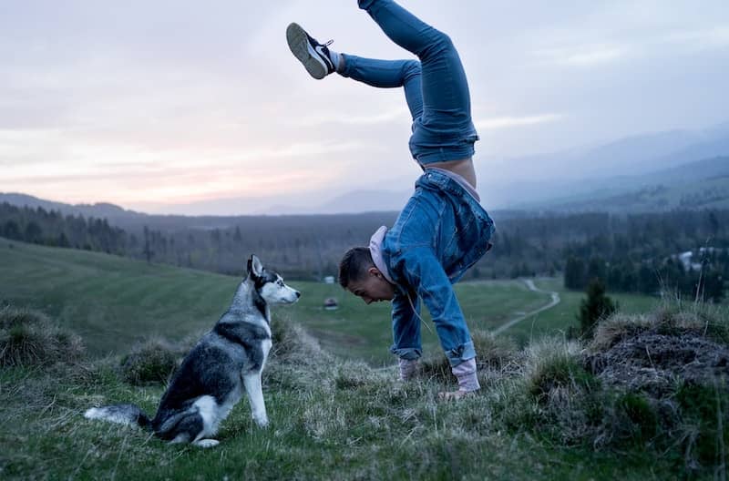 Man doing a handstand of happiness from experience minimalism benefits. Dog looks on.