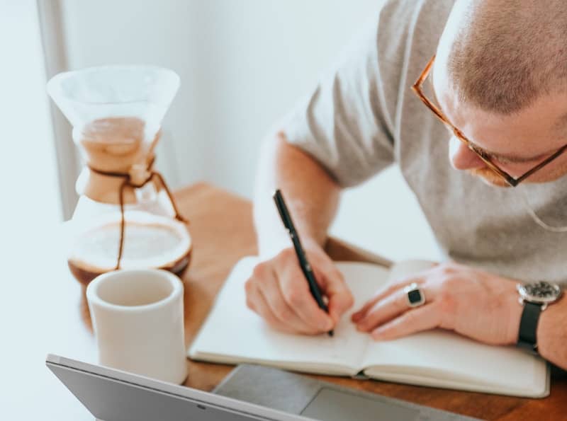 Man drinking coffee and writing in journal